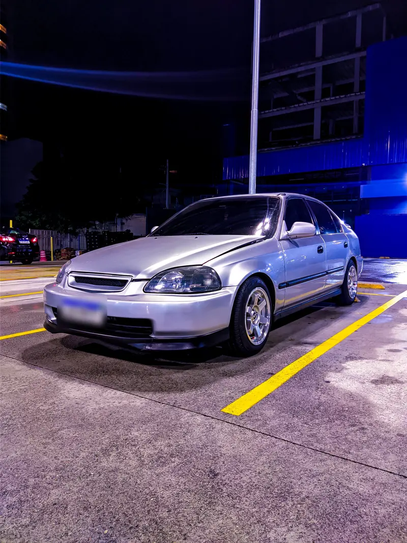 Honda Civic prata estacionado à noite, em um estacionamento com faixas amarelas