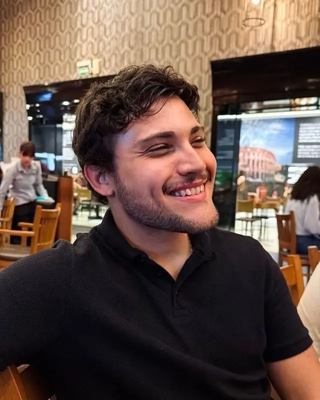 Fillipe Alves sorrindo, de camisa polo preta, sentado em um restaurante